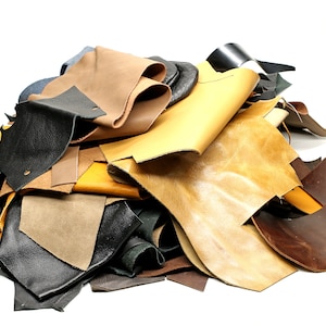 Op de afbeelding: Een stapel leerresten in verschillende kleuren, waaronder bruin, zwart, geel en beige. Het leer is in verschillende vormen en maten geknipt.