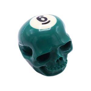May include: A green skull-shaped object with a white billiard ball on top. The billiard ball has the number "6" printed on it.