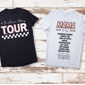 May include: Two t-shirts with text on a wooden background. One black t-shirt says "The Dance Mom TOUR" in pink and white. The other white t-shirt says "MAMA makes it all happen" with a list of roles below.