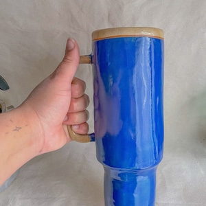 Puede incluir: Una taza de cerámica azul alta con una asa ancha y un borde beige. La taza tiene una base ligeramente acampanada.