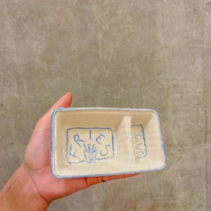 Könnte beinhalten: Eine rechteckige Keramikschale mit blauem Rand und Innenteilern. Der linke Bereich trägt das Wort "FRIES" und eine Zeichnung von Pommes Frites. Der rechte Bereich trägt das Wort "SAUCE". Die Schale ist cremefarben mit blauen Buchstaben.