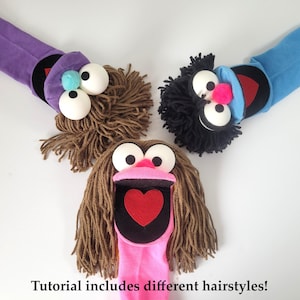 May include: Three sock puppets with yarn hair, large white ping pong ball eyes, and felt mouths. One puppet has a purple sock, one blue, and one pink. The pink puppet features a red heart inside its mouth. Text reads: Tutorial includes different hairstyles!