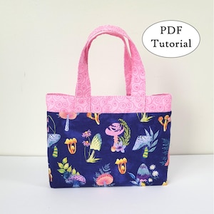 May include: A small tote bag with a pink handle and trim, featuring a dark blue fabric with a colorful mushroom pattern. The bag has a rectangular shape and the text "PDF Tutorial" is visible.