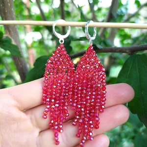 May include: A pair of red crystal beaded dangle earrings with silver hoops. The earrings are made with small, faceted beads that create a cascading effect.