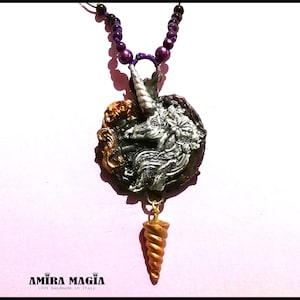 May include: A silver and gold unicorn pendant necklace with a purple beaded chain. The pendant features a detailed unicorn head with a horn and a floral design. The necklace is handmade in Italy.