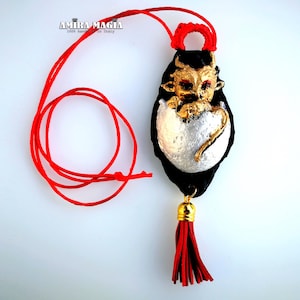 May include: A black and gold dragon pendant with red eyes, curled up inside a silver egg. The pendant is attached to a red cord with a tassel.