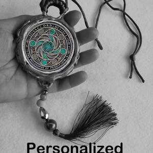 Pu&ograve; includere: Un talismano color argento con un design circolare turchese e argento, un nappa nera e il testo "Personalized Magic TALISMAN". Il ciondolo ha un cordino da indossare.