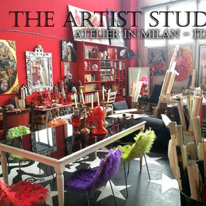 May include: A vibrant artist's studio in Milan, Italy, with red walls and eclectic decor. The space features a black table with colorful, fluffy chairs, artwork, and various art supplies. The floor has a black and white star pattern.