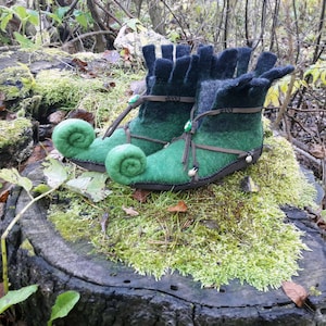 May include: A pair of green and black felt boots with curled toes. The boots have a brown leather strap and a green gem embellishment.