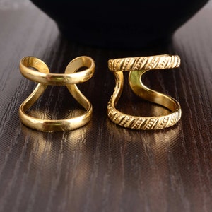 May include: Two gold-toned rings with a simple design. One ring has a smooth finish, while the other has a textured, patterned finish.