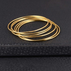 Puede incluir: Un conjunto de seis pulseras de brazalete de color dorado apiladas una encima de la otra. Las pulseras son delgadas y tienen un acabado liso y pulido.