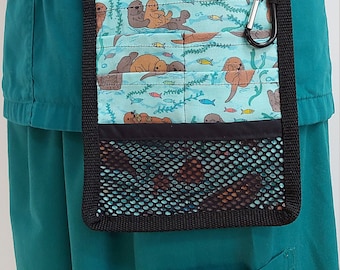 May include: A teal blue medical scrub top with a black belt and a black and teal blue utility pouch with a sea otter print and a mesh pocket. The pouch has a black carabiner clip.