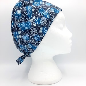 May include: A scrub cap featuring a dark blue background with a repeating pattern of light blue and white microorganisms, bacteria, and DNA strands. The cap has a fitted crown and ties at the back to secure the fabric in place around the head.