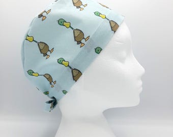 May include: A light blue surgical scrub hat with a pattern of brown ducks with green heads. The hat has a tie at the back.
