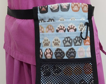 May include: A black fabric belt with a blue and white fabric pouch with paw prints. The pouch has multiple pockets and a mesh bottom. The pouch is attached to the belt with a black buckle.