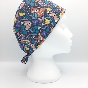 May include: A dark blue scrub hat with a colorful print of deer and bunnies in a field of flowers. The hat has a tie at the back.