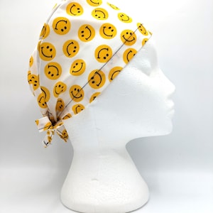 May include: White surgical scrub hat with a yellow smiley face pattern.