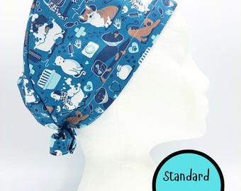 May include: A blue surgical scrub cap featuring a pattern of dogs, cats, medical tools, and paw prints. The cap is tied at the back and displayed on a white mannequin head. The text "Standard Size" is in a blue circle.