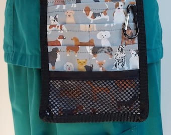 May include: A teal green scrub top with a black fabric belt and a black and grey dog-themed utility belt with a mesh pocket. The utility belt has a black carabiner clip.