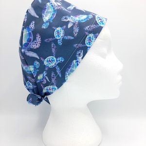 May include: A blue surgical scrub hat with a pattern of colorful sea turtles. The hat is tied at the back with a bow.