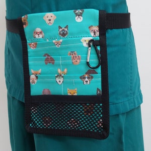 May include: A teal blue medical scrub top with a black belt and a teal blue and white patterned utility pouch with a mesh pocket and a carabiner clip.
