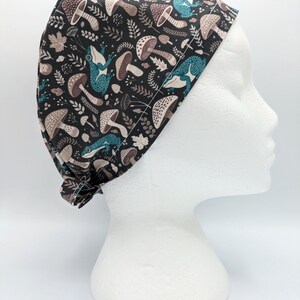 Pode incluir: Um gorro de cirurgia preto com um padrão de sapos azuis, cogumelos e folhas.