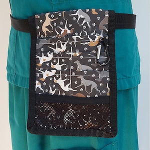 May include: Black dog walking belt bag with a black strap and a silver carabiner clip. The bag has a black mesh pocket and a patterned fabric with greyhounds and paw prints.