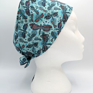 Puede incluir: Un gorro de quirófano azul turquesa con un patrón de libélulas. El gorro tiene un lazo en la parte posterior.