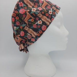 Peut inclure: Un bonnet de travail noir avec un imprimé floral représentant des chiens bruns et des fleurs roses. Le bonnet a un lien à l'arrière.
