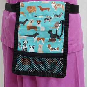 Puede incluir: Un cinturón de utilidad de tela turquesa y negro con un bolsillo de malla y un estampado de perro. El cinturón tiene un clip negro y se lleva alrededor de la cintura.