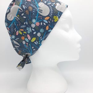 Può includere: Un berretto chirurgico blu con un motivo di bradipi e fiori. Il berretto ha un laccio sul retro.