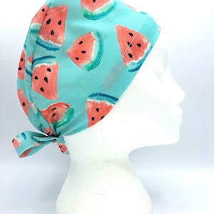 Puede incluir: Un gorro de quirófano azul turquesa con estampado de sandía. El gorro tiene un lazo en la parte posterior.