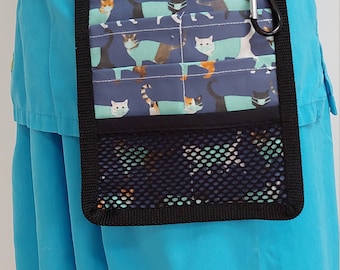 May include: A blue scrub top with a black belt and a black and blue cat-themed utility pouch with a mesh pocket. The pouch has a zipper and a carabiner clip.