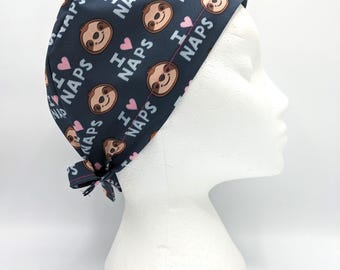May include: A dark blue scrub hat with a repeating pattern of sloths and the text "I love naps". The sloths are brown with pink hearts and white eyes.