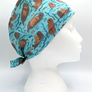 Könnte beinhalten: Eine blaue OP-Mütze mit einem Muster aus Seeottern und Fischen. Die Mütze hat einen Bindfaden an der Rückseite.