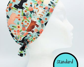 May include: A light blue scrub cap featuring a pattern of farm animals and orange flowers. The cap is tied at the back and displayed on a mannequin head. The text "Standard Size" is in a teal circle.