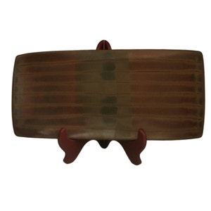 May include: A rectangular ceramic serving tray with a brown, green, and red striped pattern. The tray is on a red stand.