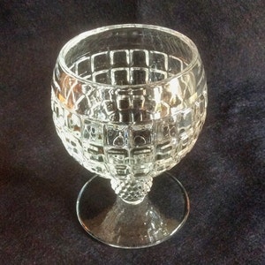 May include: A clear glass goblet with a geometric pattern on the bowl and a short stem. The goblet has a round base.