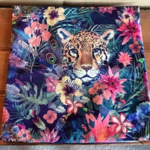 May include: A dark blue throw pillow with a colorful tropical print featuring a jaguar, flowers, and feathers.