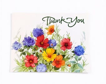 Puede incluir: Una tarjeta de felicitación rectangular con el texto Thank You en letra cursiva verde oscuro sobre una vibrante ilustración en acuarela de varias flores, incluyendo pétalos rojos, amarillos, naranjas y azules con tallos verdes.