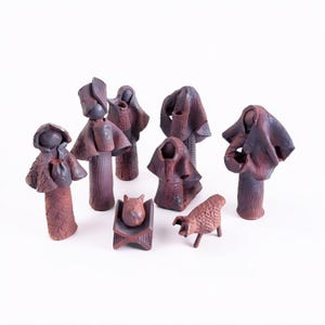 May include: A set of eight dark reddish-brown clay figurines depicting a nativity scene. The collection includes several standing figures with draped garments, a small figure resting in a rectangular cradle, and a four-legged animal figure.