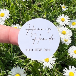 May include: White round sticker with black text that says "Hana's Hen do 14th June 2024".