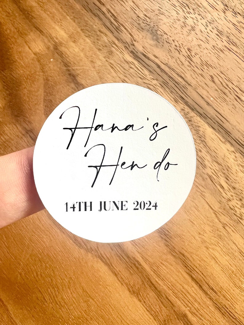 May include: White round sticker with black text that reads "Hana's Hen do 14th June 2024".