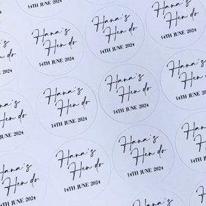 May include: A sheet of white paper with multiple round stickers. Each sticker has black calligraphy that reads "Hana's Hen do" and the date "14TH JUNE 2024".