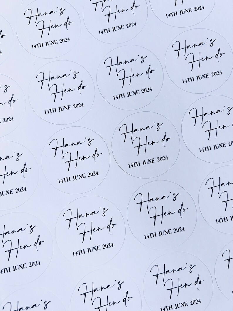 May include: A sheet of white paper with multiple round stickers. Each sticker has black calligraphy that reads "Hana's Hen do" and the date "14TH JUNE 2024".