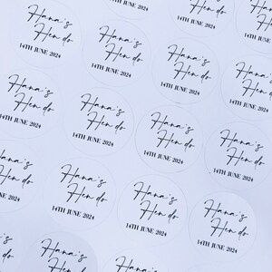 May include: A collection of white round stickers with black text that says "Hana's Hen do" and the date "14th June 2024".