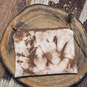 Könnte beinhalten: Eine braune und weiße Batik-Clutch mit Reißverschluss auf einer Holzoberfläche.