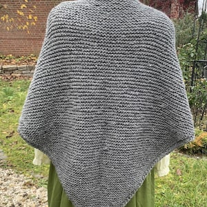 Może przedstawiać: Szary, dziergany szal w kształcie trójkąta. Szal wykonany jest z miękkiej, fakturowanej przędzy i ma prosty, elegancki wzór.