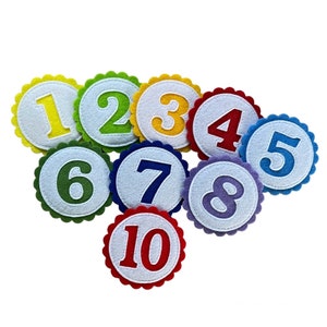 Könnte beinhalten: Zehn bunte Filz-Kreise mit weißen Zentren und den Zahlen 1 bis 10 in verschiedenen Farben.