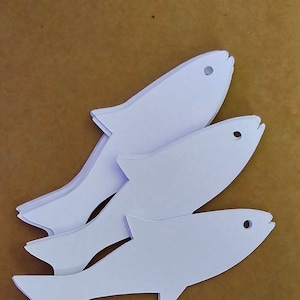 May include: Three white paper fish cutouts stacked on top of each other. The fish are all the same shape, but different sizes. The largest fish is at the top of the stack, and the smallest fish is at the bottom.